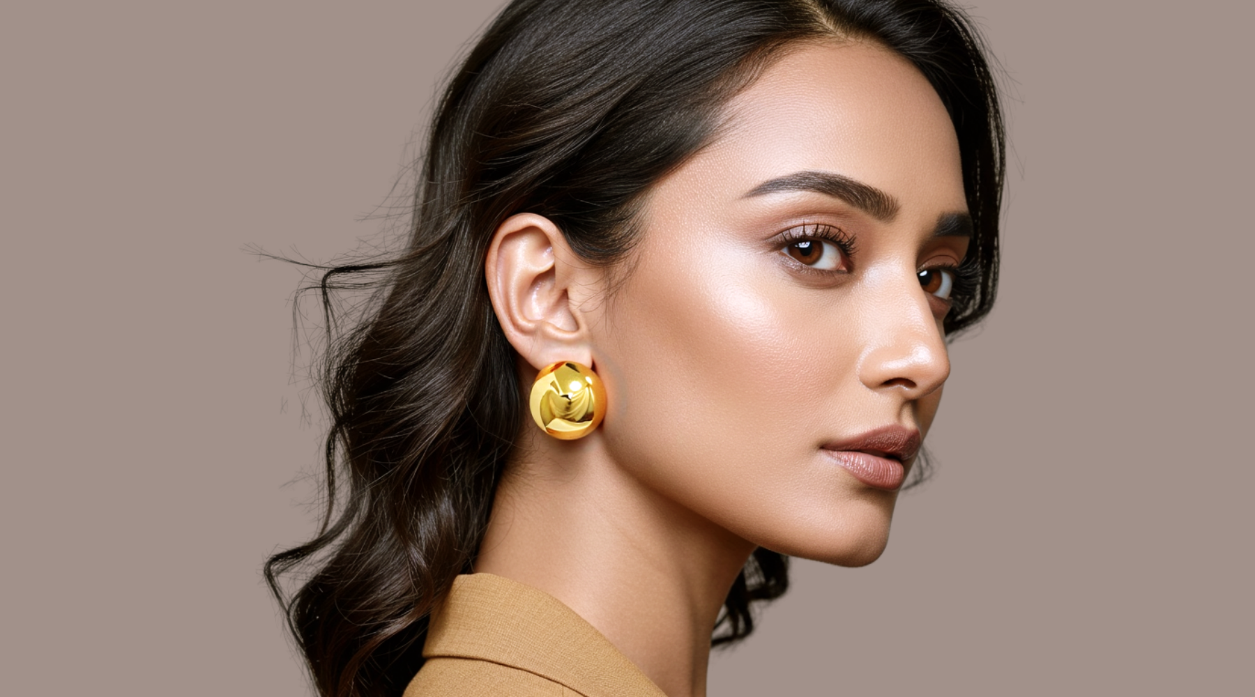 Woman wearing gold earrings against a beige background