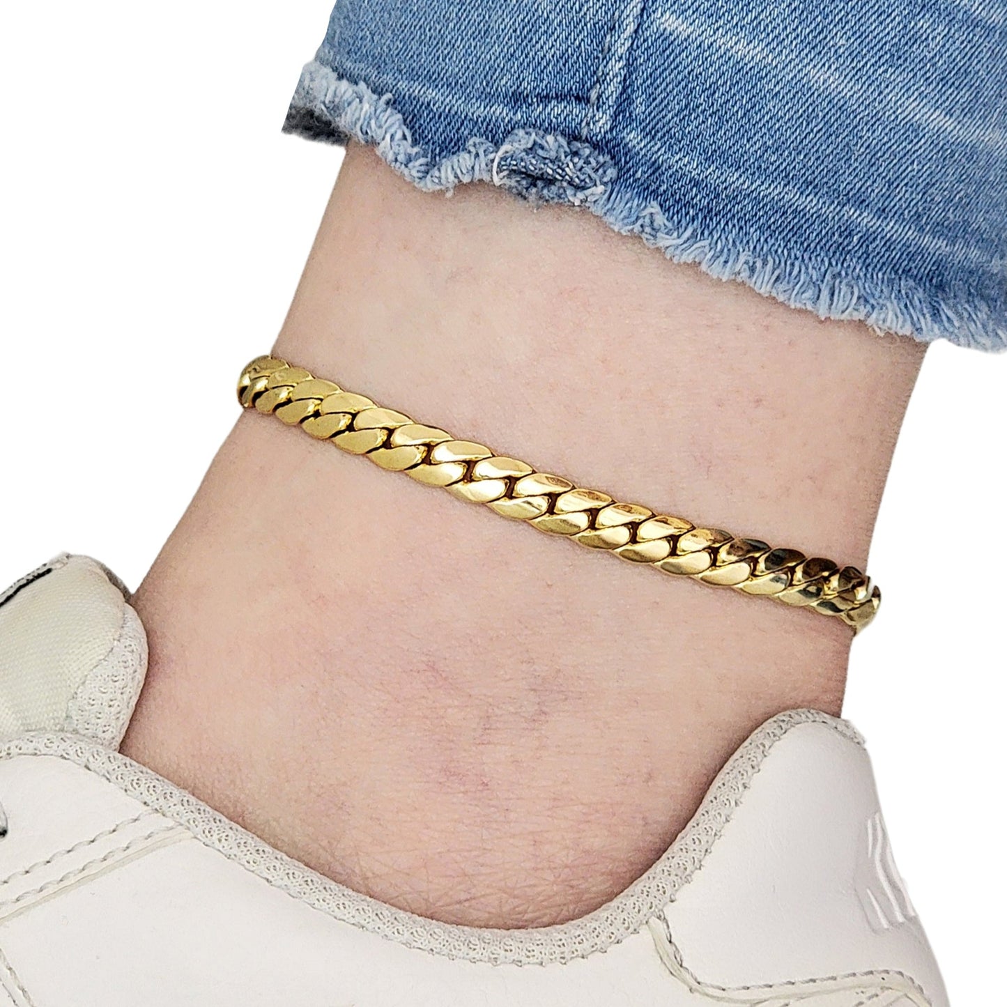 Gold chain anklet on a person's ankle with denim shorts and white sneakers.
