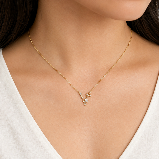 A delicate gold necklace with a small V-shaped pendant featuring tiny clear stones, worn by a model in a white V-neck top.
