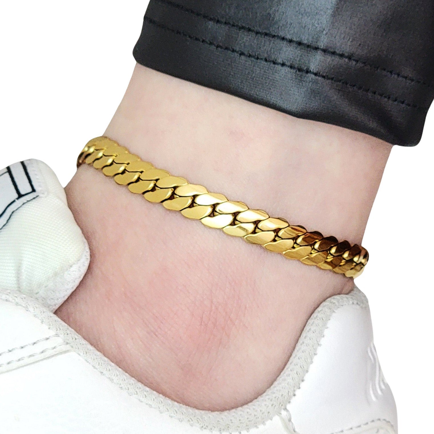 Gold chain anklet on a person's ankle with a white sneaker and black pants.
