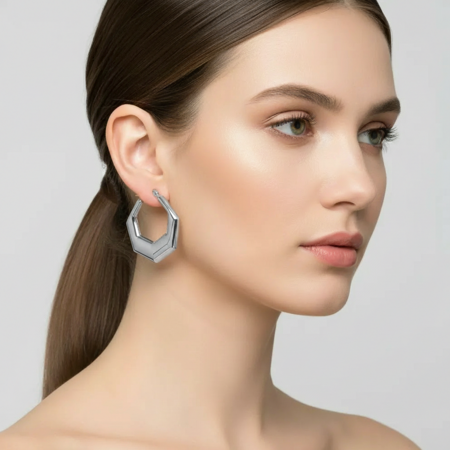 Woman wearing a silver hoop earring against a neutral background
