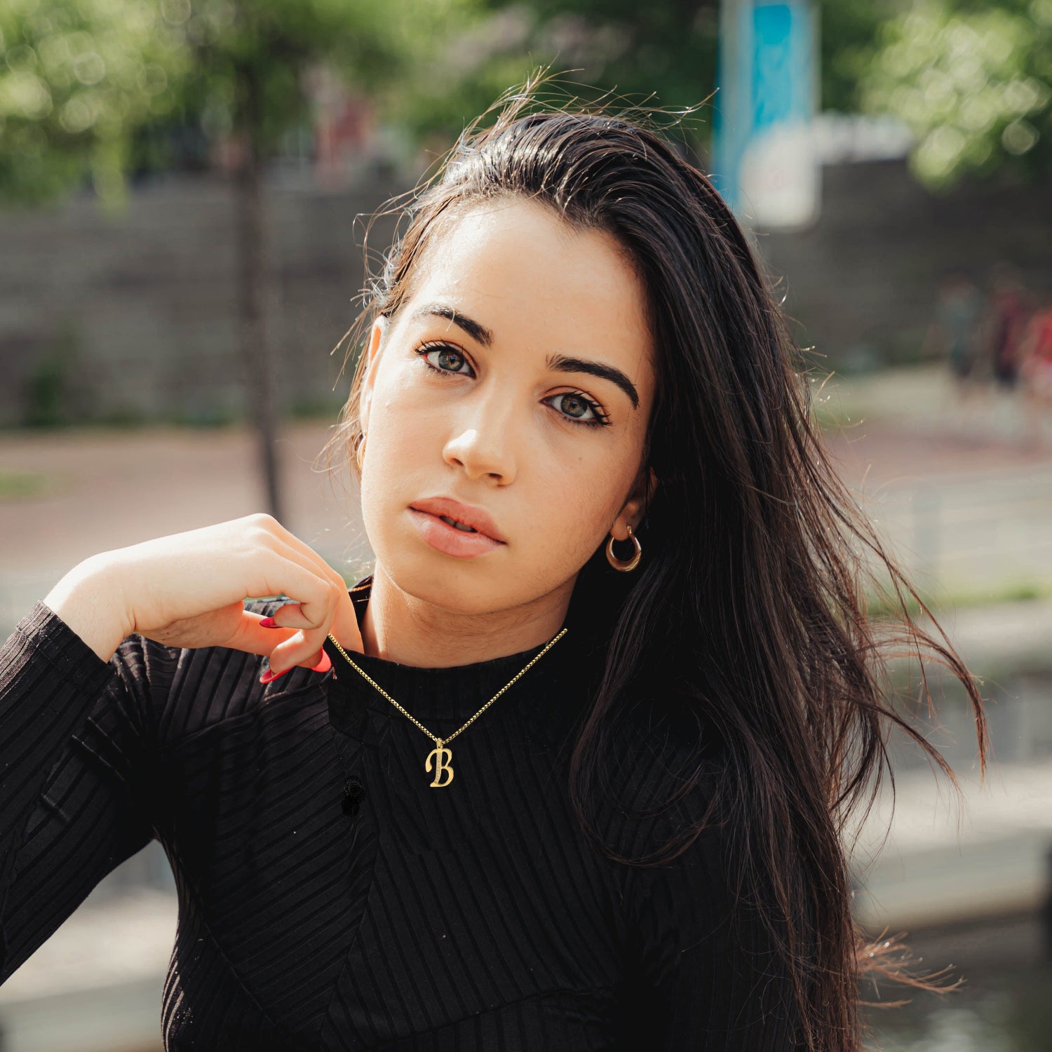 Woman wearing a black sweater and gold necklace by a body of water