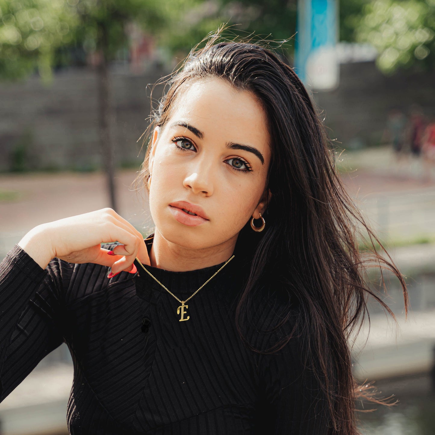 Woman wearing a E Necklace black sweater with a blurred outdoor background