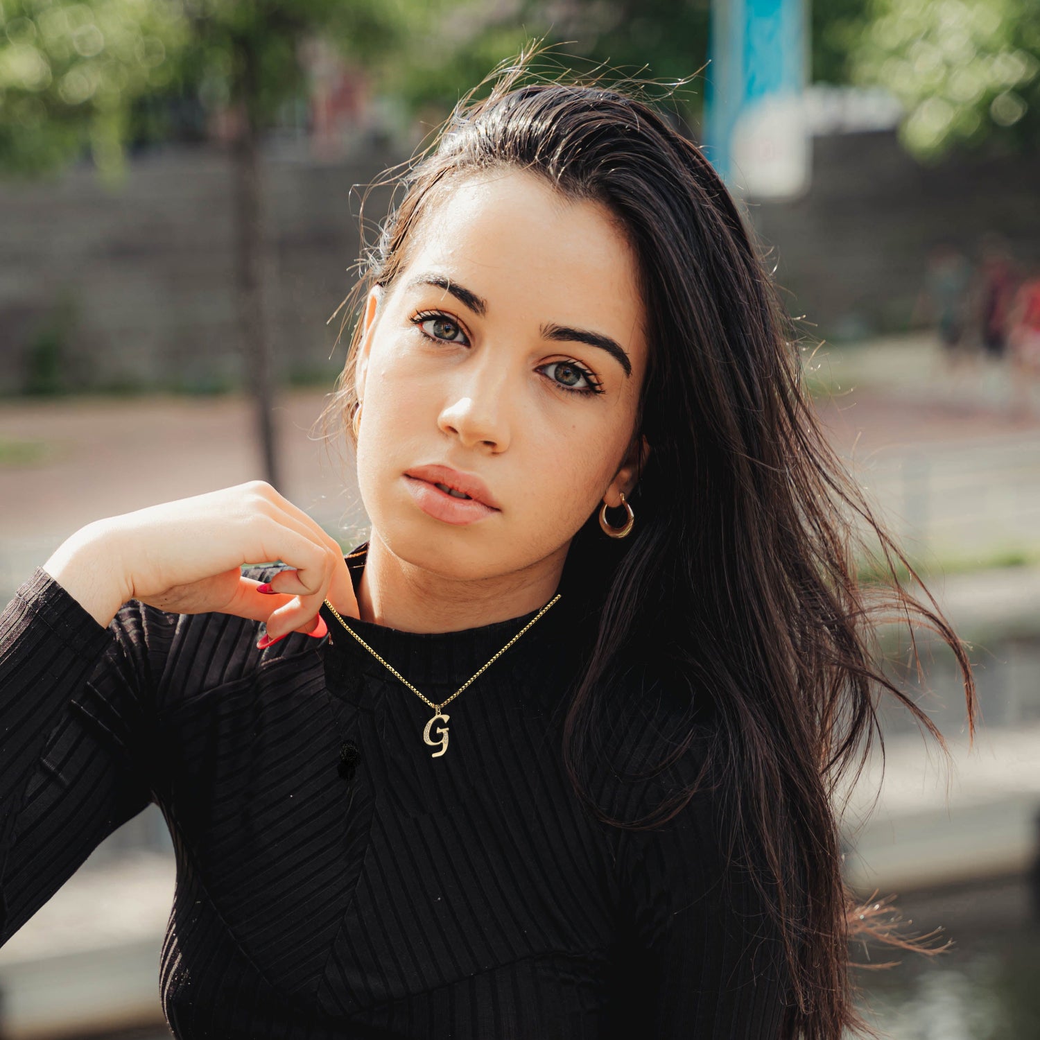 Woman wearing G Necklace black sweater with a blurred outdoor background