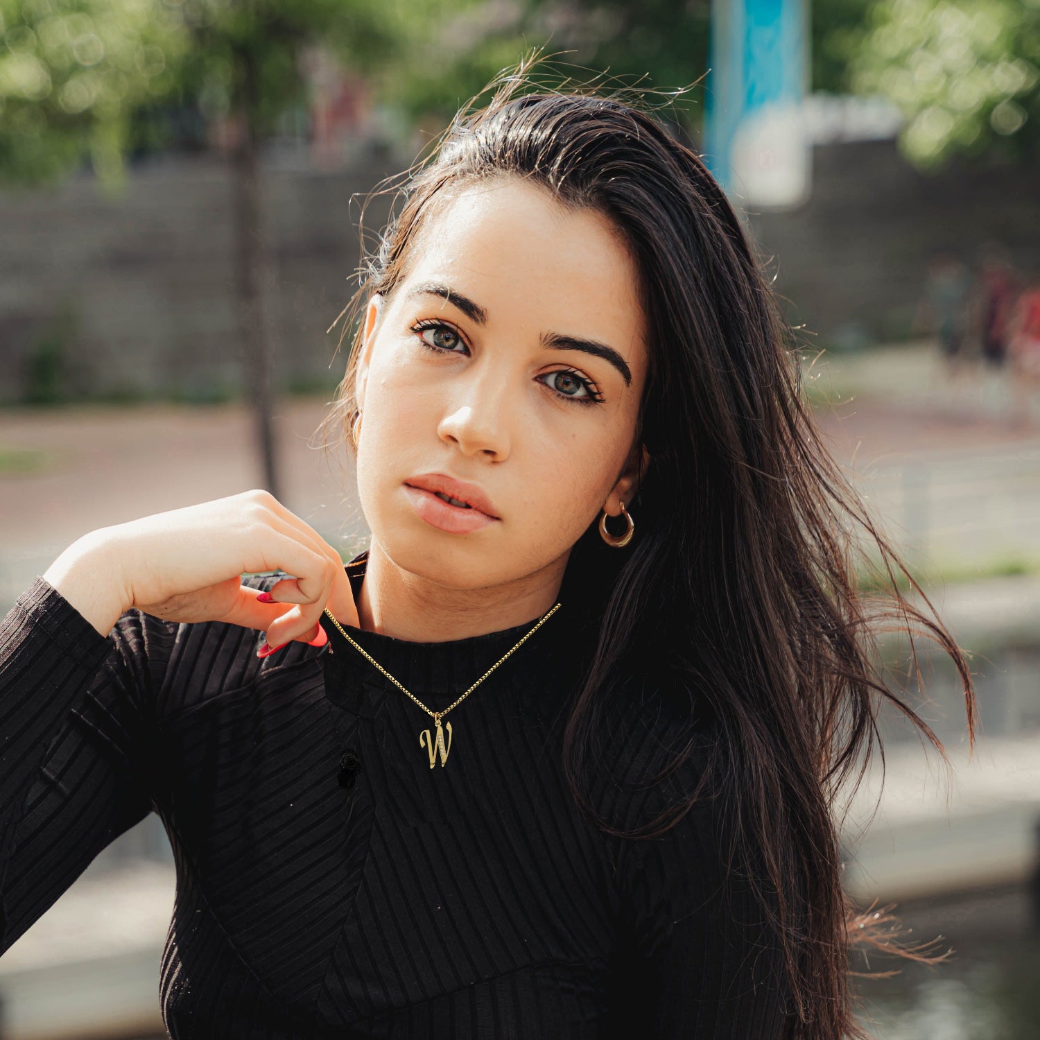 Woman wearing a W Necklace black sweater with a blurred outdoor background