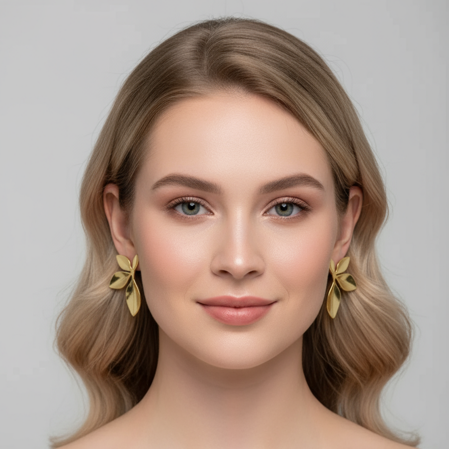 Woman with styled hair and gold bow earrings against a neutral background