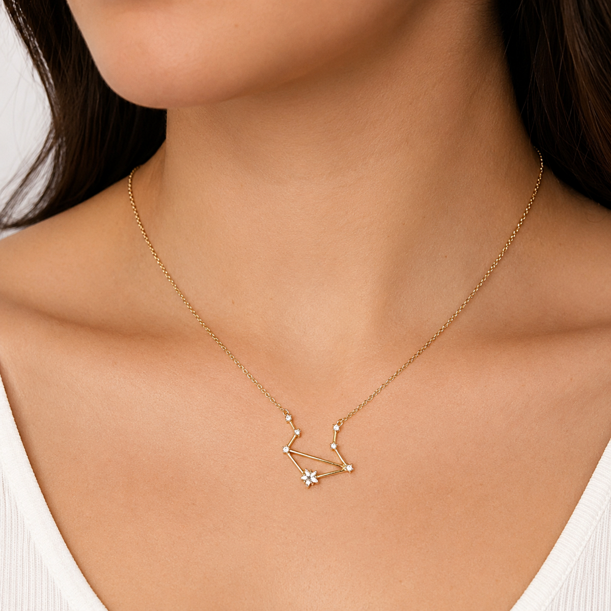A delicate gold necklace with a constellation pendant featuring a small clear gemstone, worn on a model's neck.