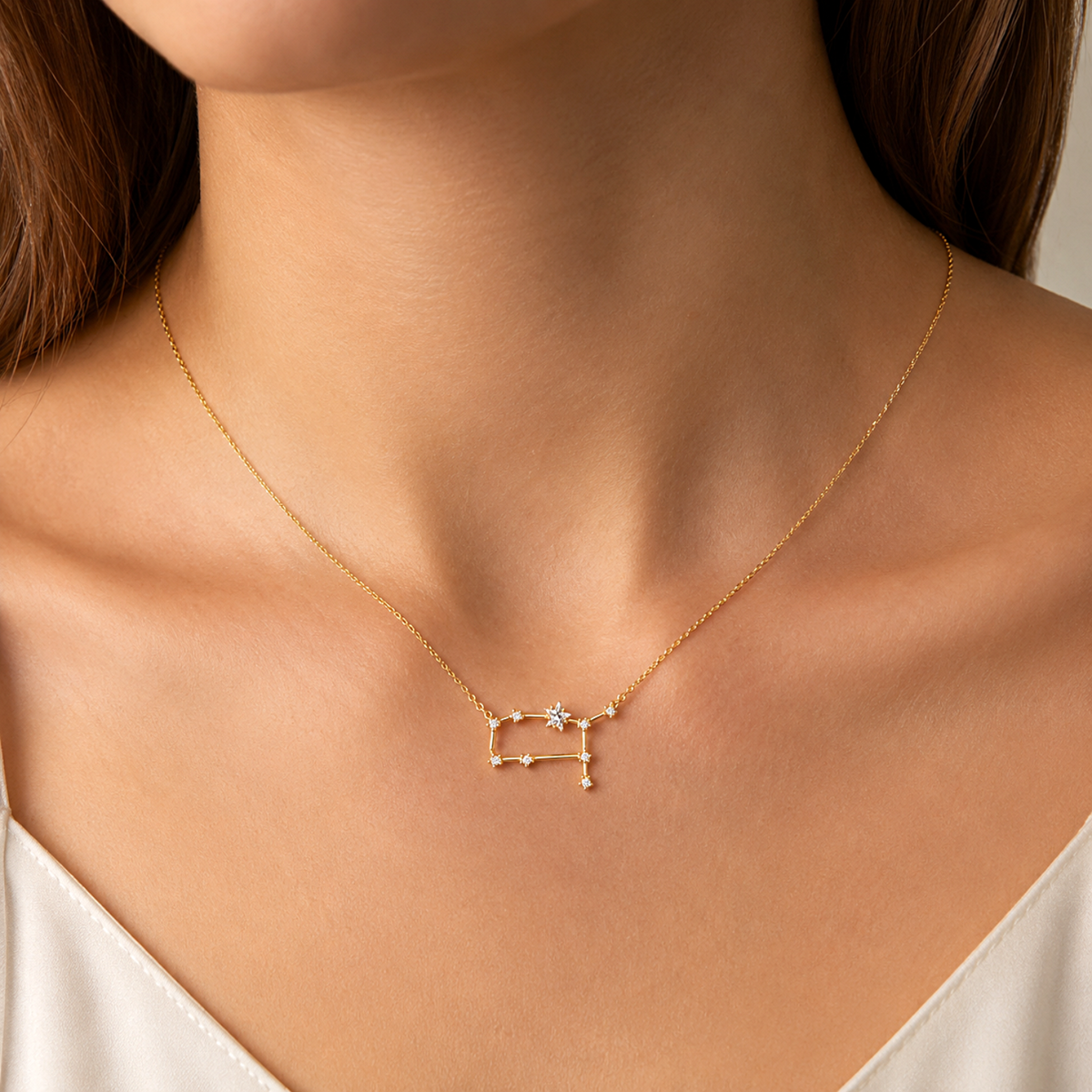 A delicate gold necklace with a zodiac sign pendant representing Libra, worn by a model. The pendant features a small gold Libra constellation outline with a tiny clear gemstone at the center.