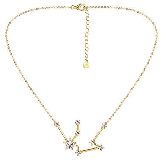 A gold necklace featuring a constellation pendant adorned with clear crystals, displayed on a clean white background. The necklace includes an adjustable clasp chain with a small circular 'SB' brand tag.