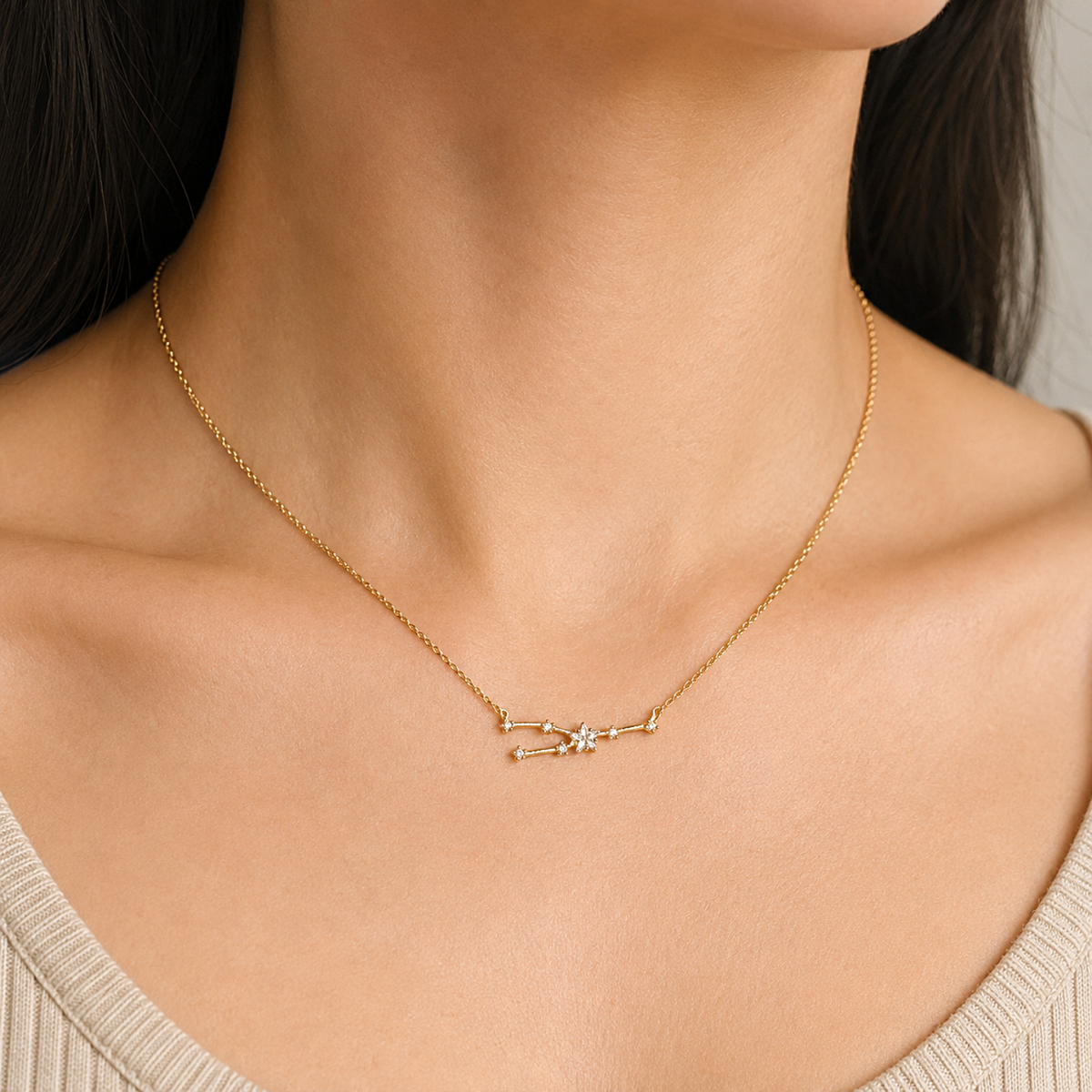 A close-up of a model's neck and upper chest wearing a delicate gold chain necklace with a small geometric pendant featuring a central clear gemstone.