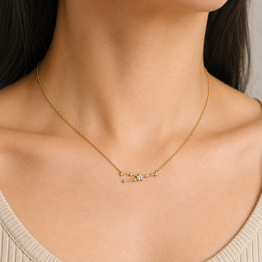 A close-up of a model's neck and upper chest wearing a delicate gold chain necklace with a small geometric pendant featuring a central clear gemstone.