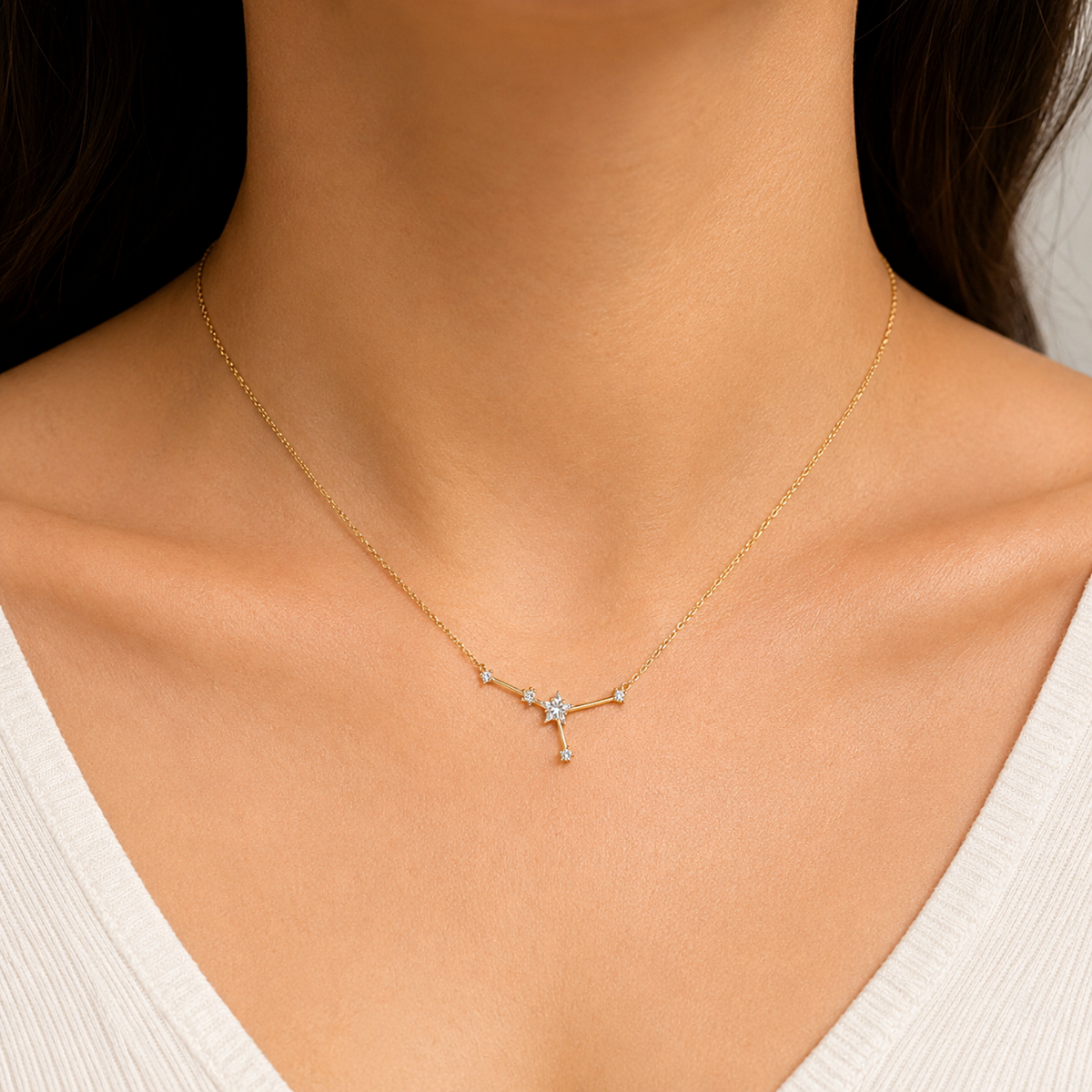 A delicate gold necklace with a small star and branch-like pendant, worn on a model's neck over a white ribbed V-neck top.