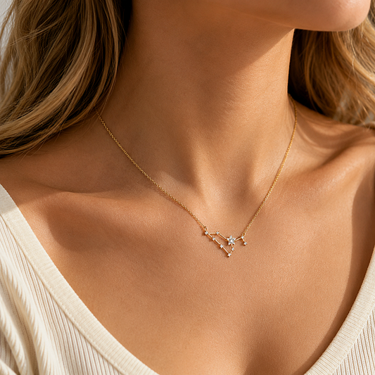 A close-up lifestyle shot of a woman wearing a delicate gold chain necklace with a geometric starburst pendant set with small clear stones, styled with a cream ribbed top.