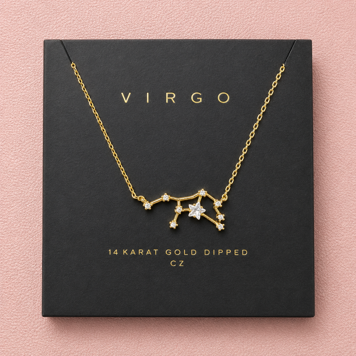 A gold Virgo constellation necklace with clear cubic zirconia stones, presented on a black gift box with gold lettering against a textured pink background.