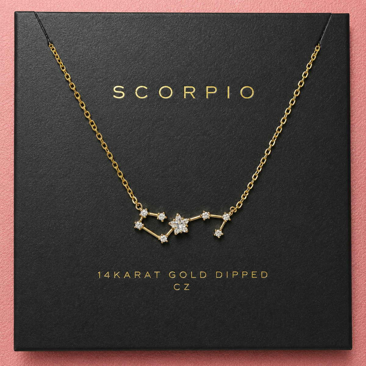 A gold necklace with a Scorpio constellation pendant made of clear stones, presented on a black gift box with gold lettering that reads 'SCORPIO' and '14KARAT GOLD DIPPED CZ'.
