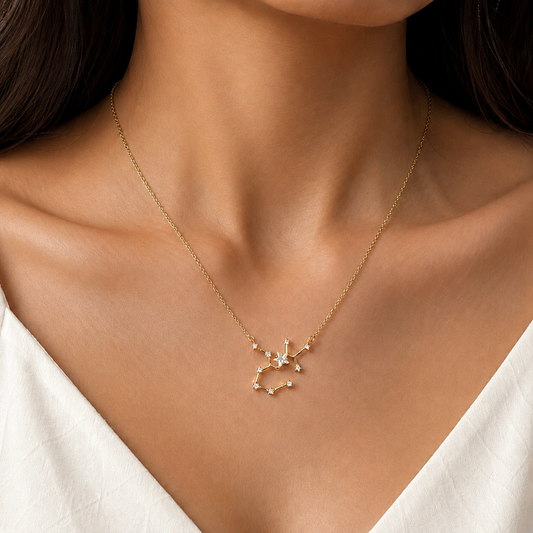 A delicate gold chain necklace with a small constellation pendant, worn on a model's neck over a white top.