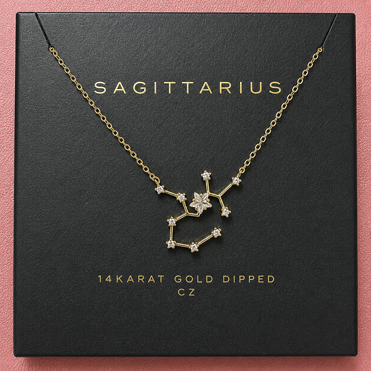 A gold necklace with a constellation pendant, displayed on a black square box printed with the brand name 'SAGITTARIUS' and text reading '14KARAT GOLD DIPPED CZ'.