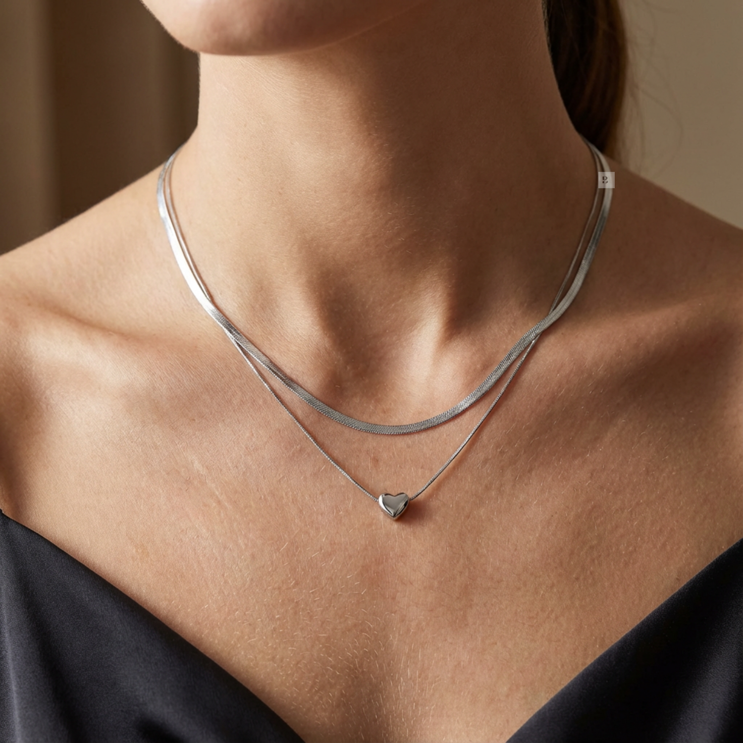 Silver necklace with a heart pendant on a person wearing a black top.