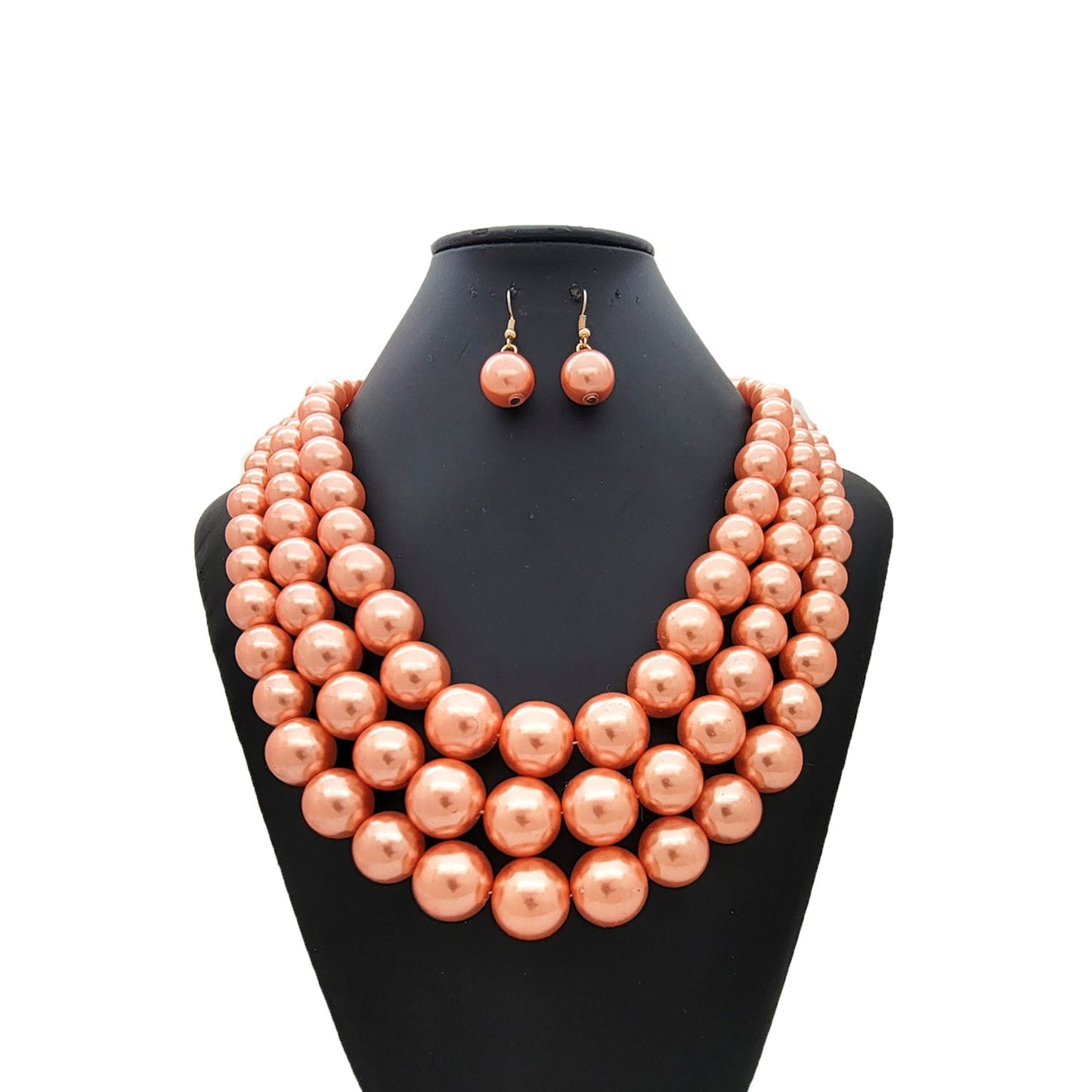 Peach-colored pearl necklace and earrings on a black mannequin bust against a white background