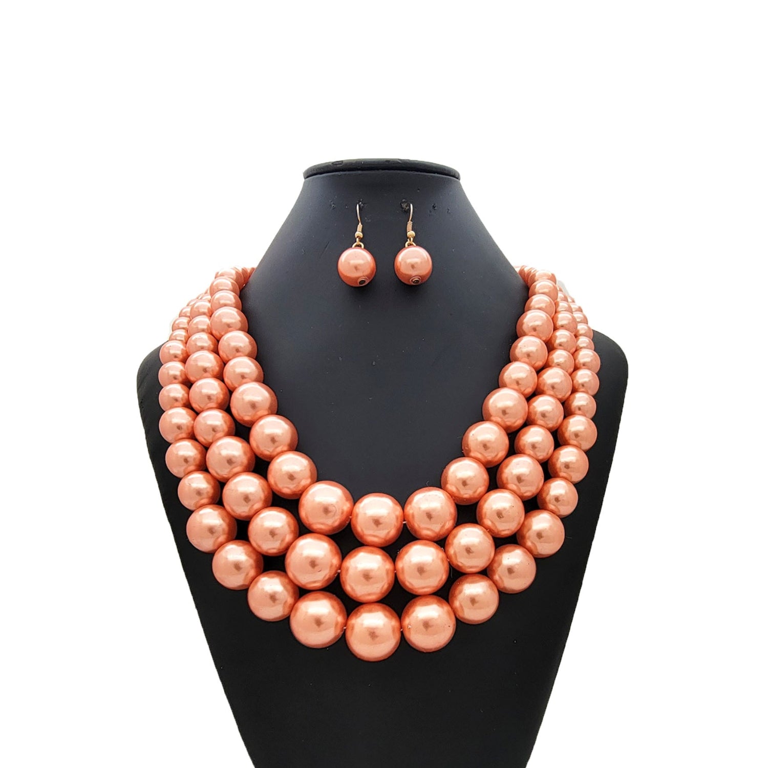 Peach-colored pearl necklace and earrings on a black mannequin bust against a white background