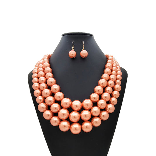 Peach-colored pearl necklace and earrings on a black mannequin bust against a white background