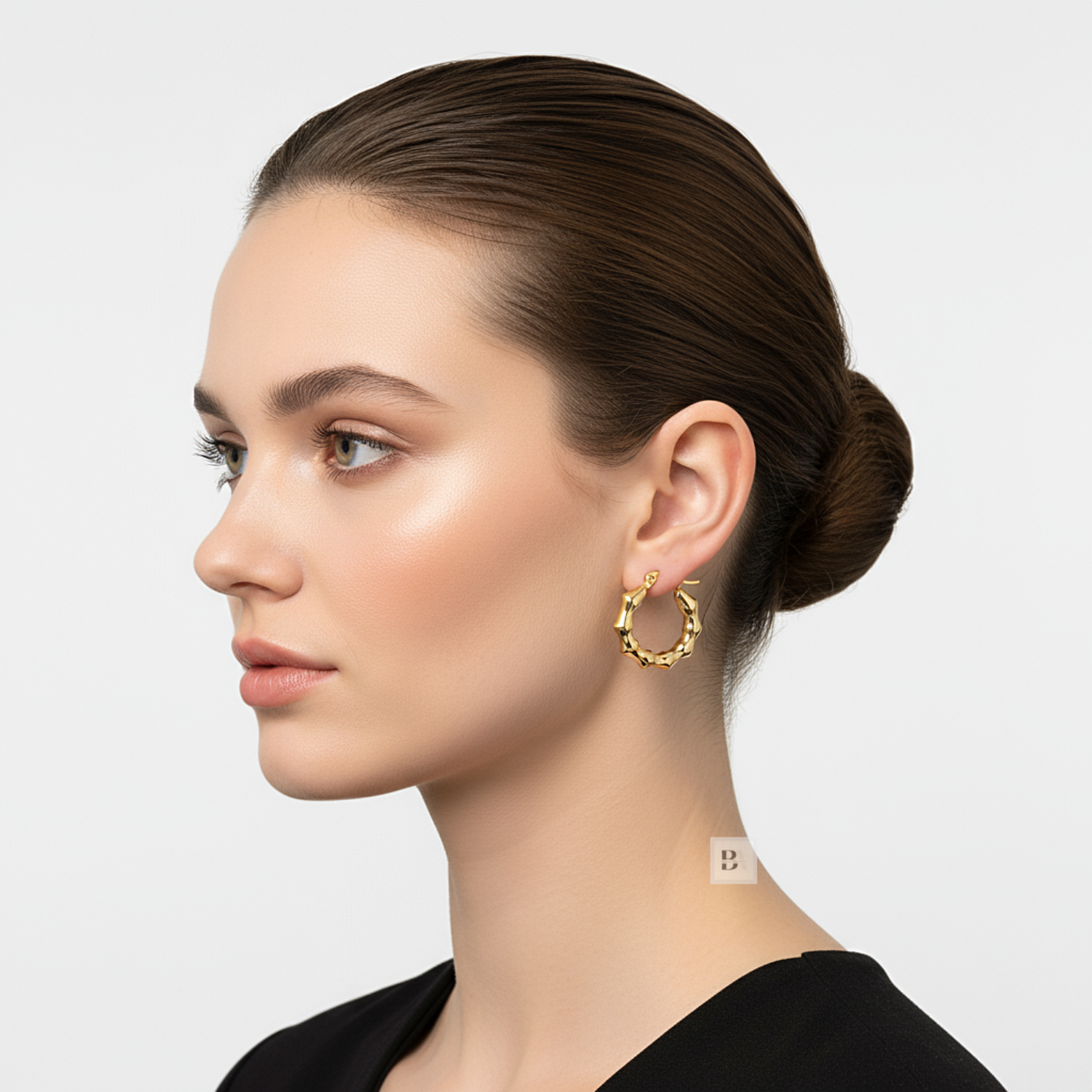 Woman wearing gold hoop earrings on a plain background