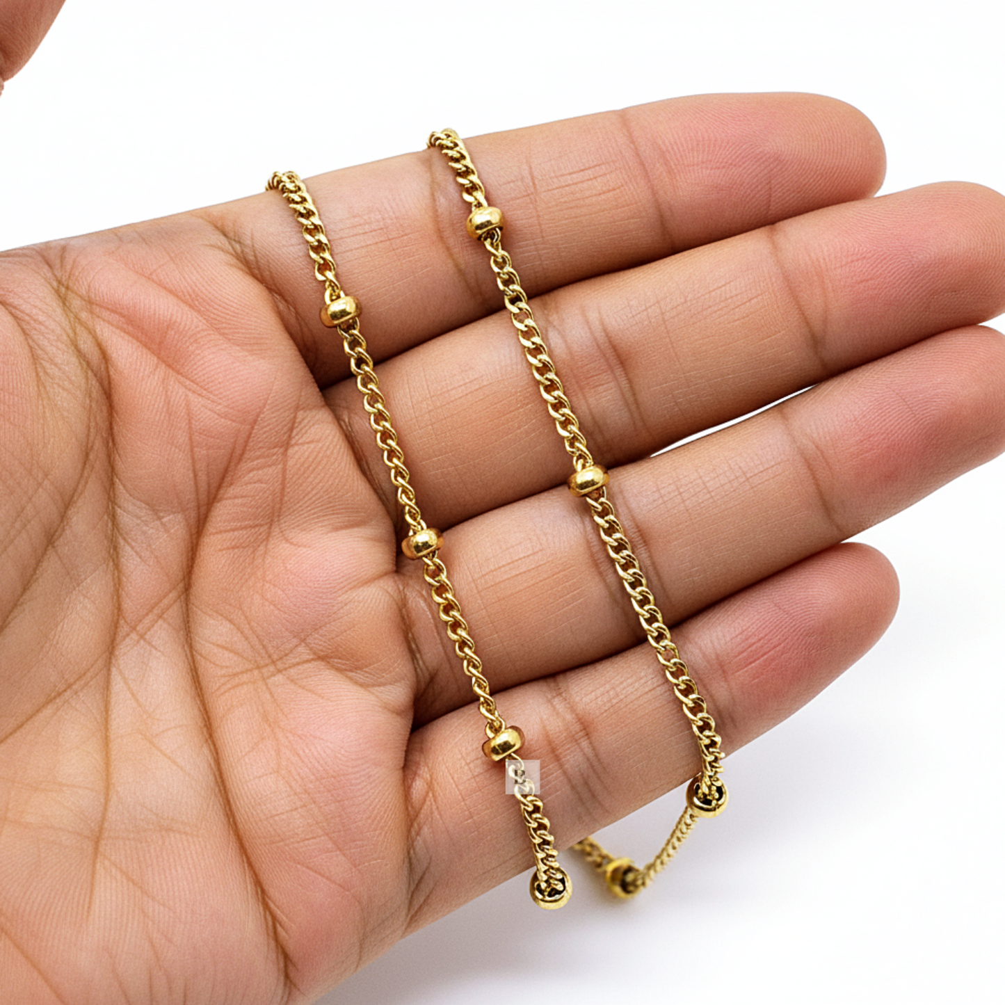 Gold chain necklace held in a hand against a white background