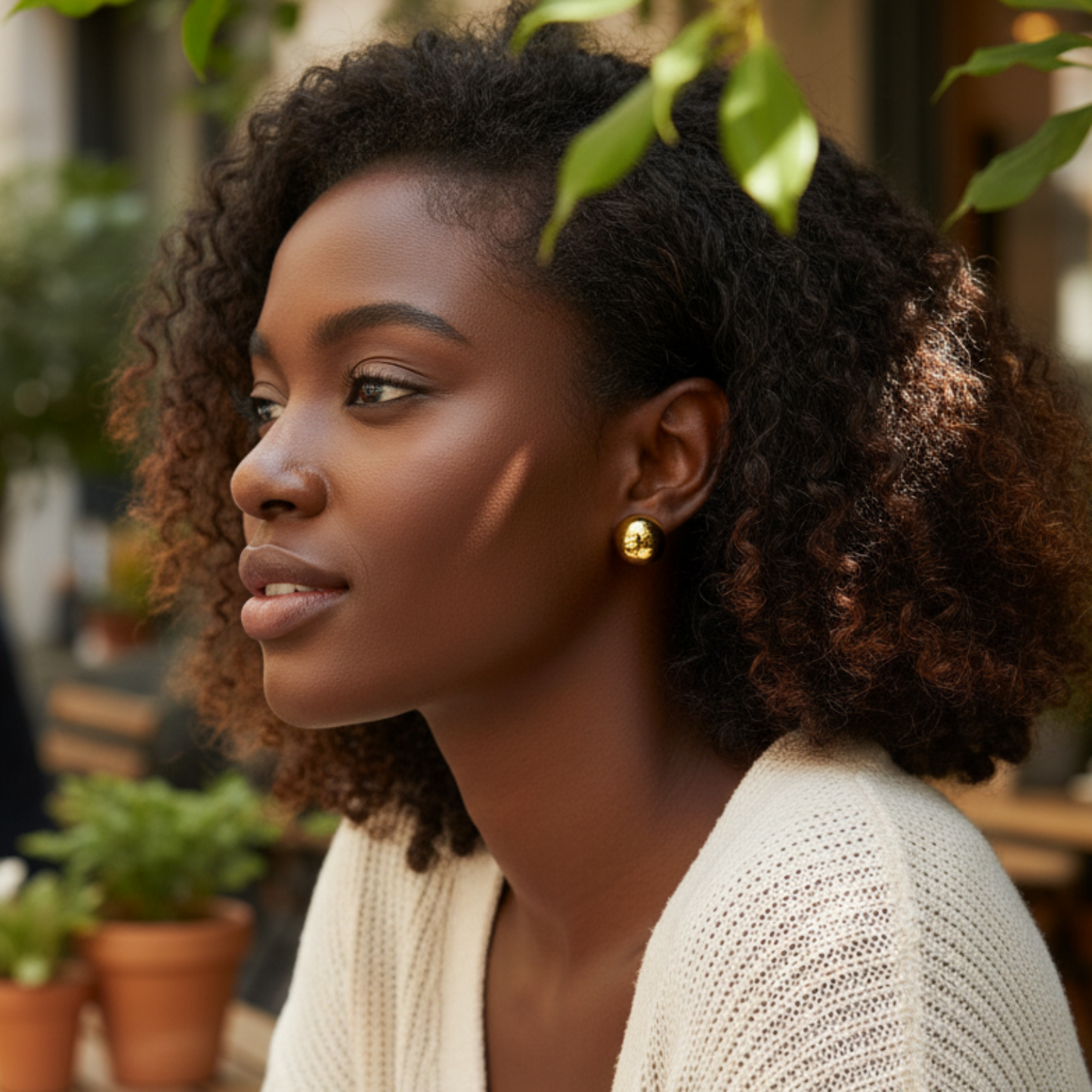 Woman sitting outdoors wearing a beige cardigan with plants and people in the background