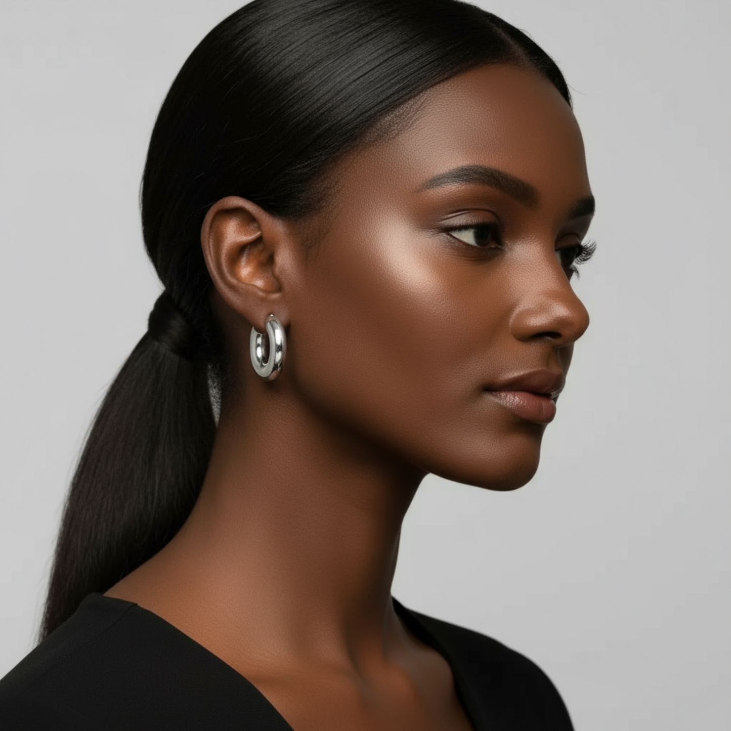 Woman with a side ponytail wearing earrings against a neutral background