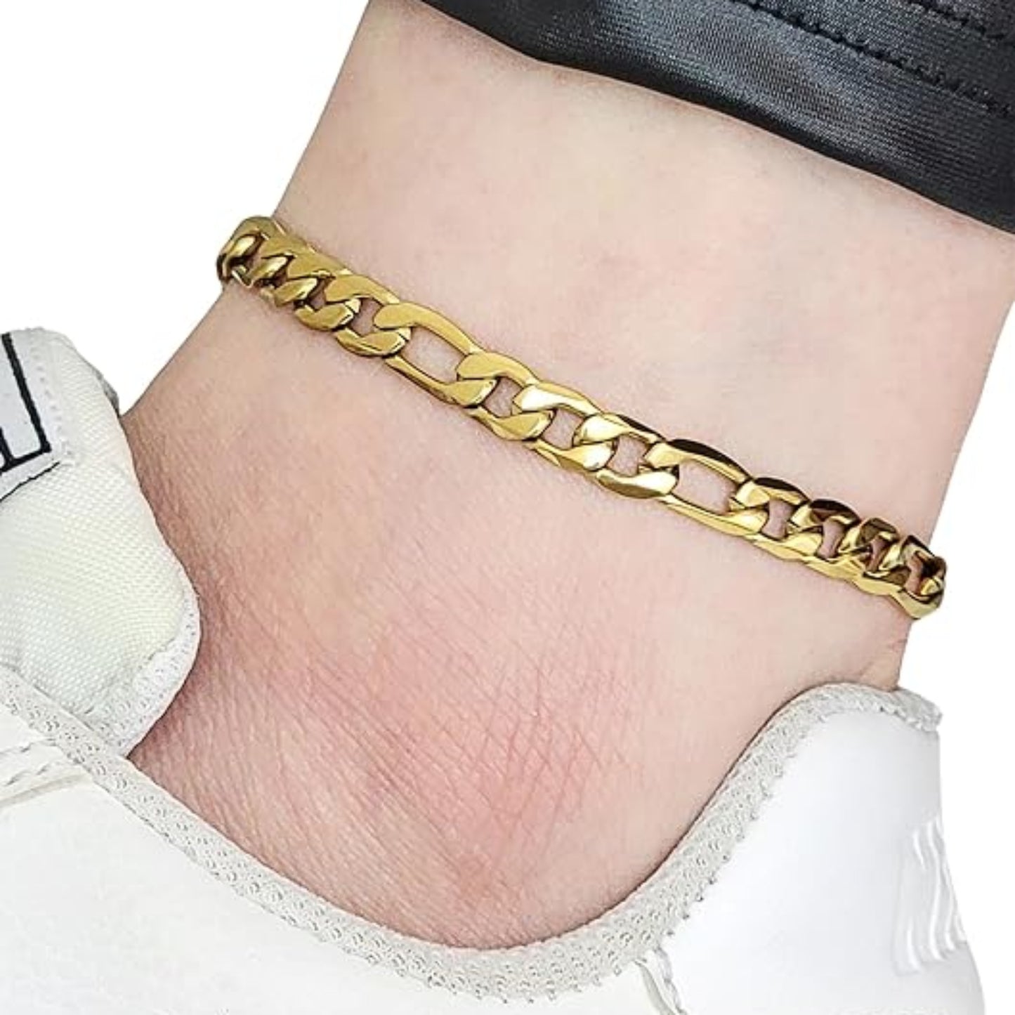 Gold chain bracelet on a ankle with a white sneaker and black pants.