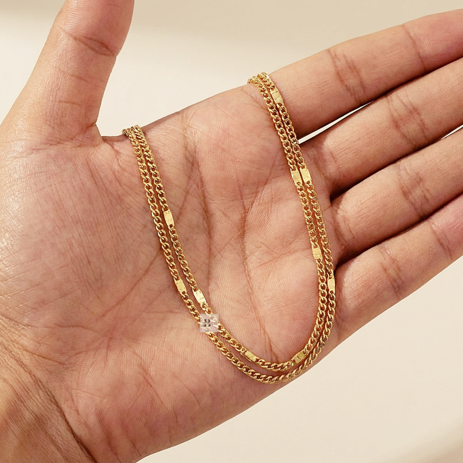 Gold chain anklet with a diamond pendant held in a hand against a neutral background