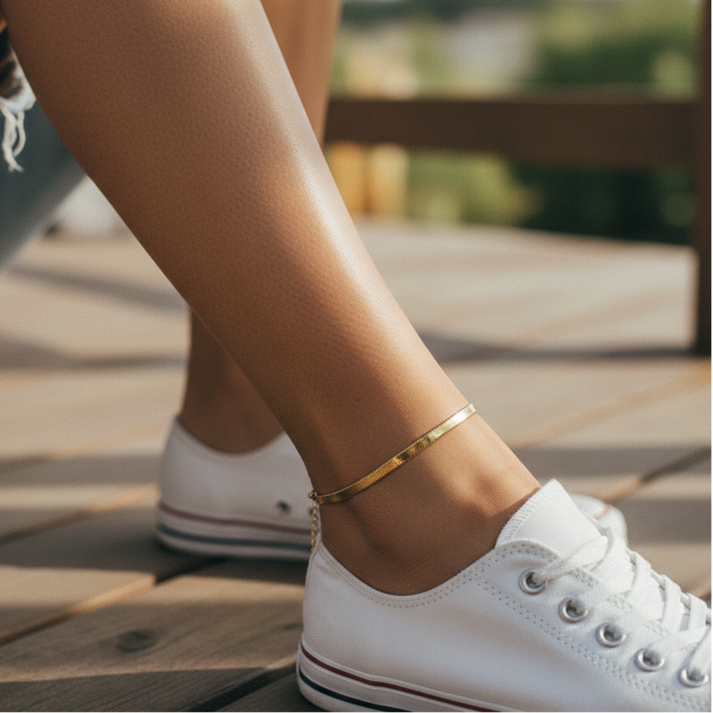 Person wearing white sneakers with a gold anklet on a wooden deck.
