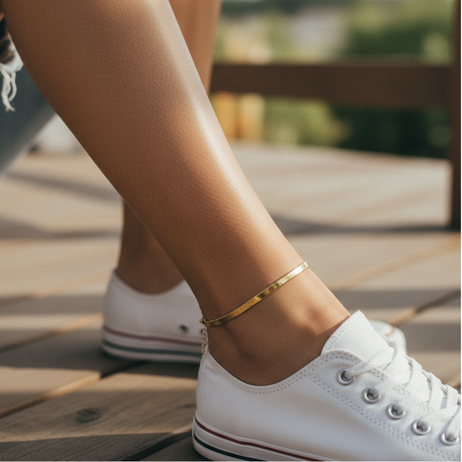 Person wearing white sneakers with a gold anklet on a wooden deck.