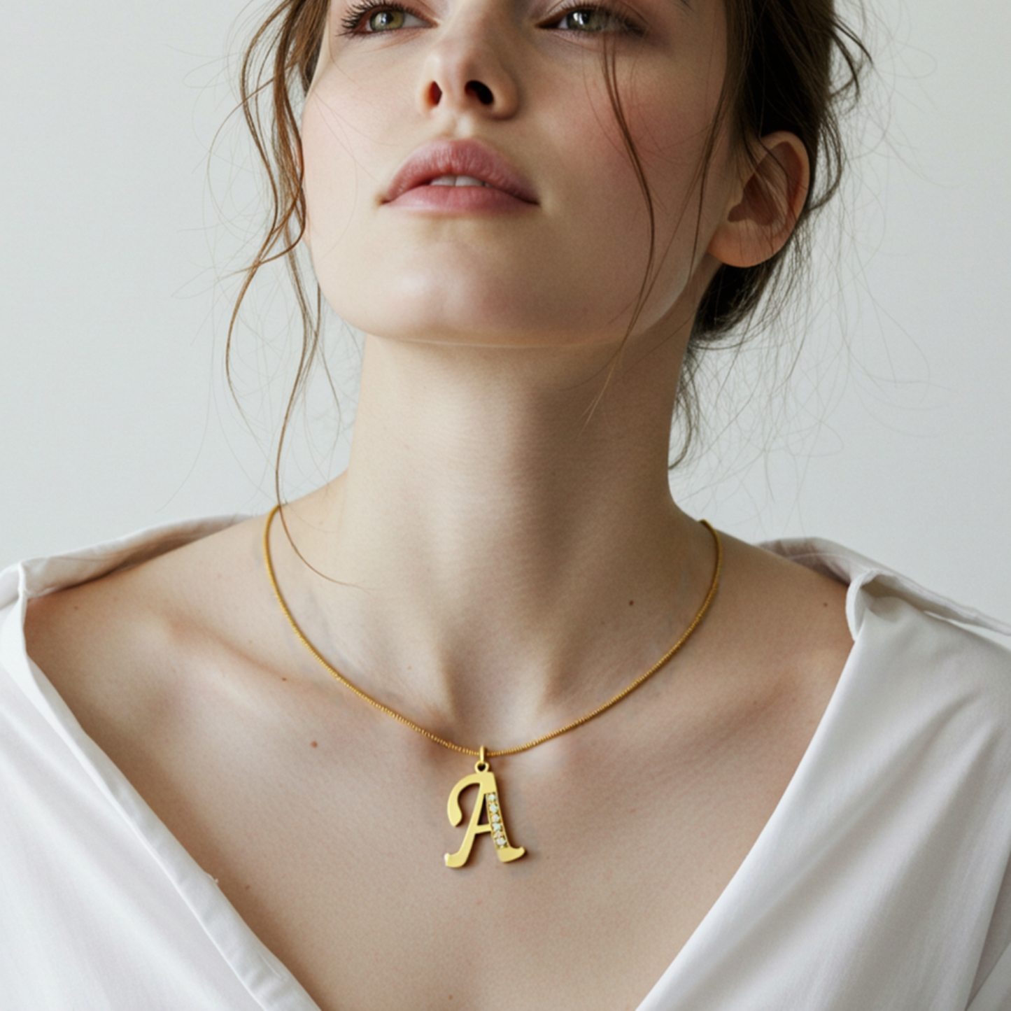 Woman wearing a gold necklace with a 'A' pendant against a neutral background