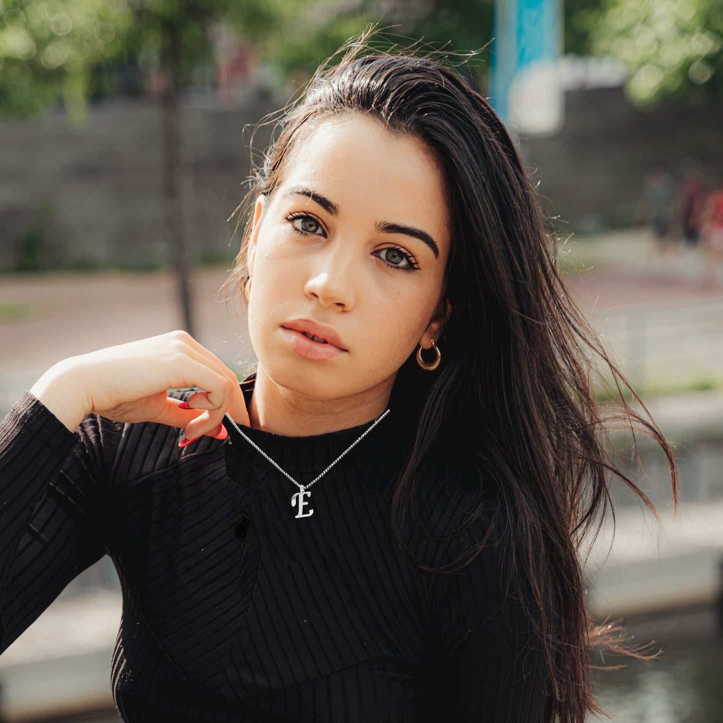 Woman wearing E Necklace black ribbed sweater with a blurred outdoor background