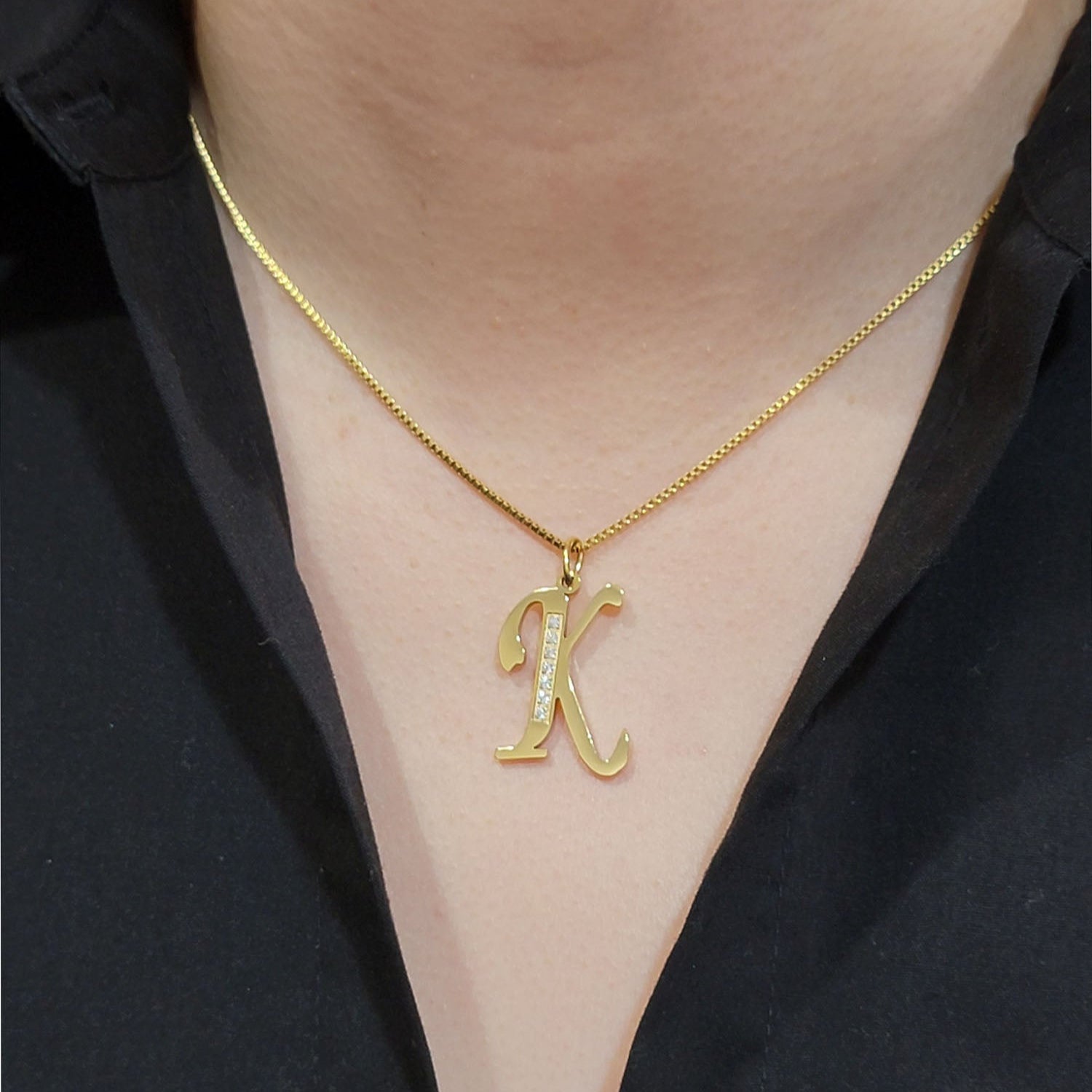 Gold necklace with a 'K' pendant worn by a person against a black shirt background