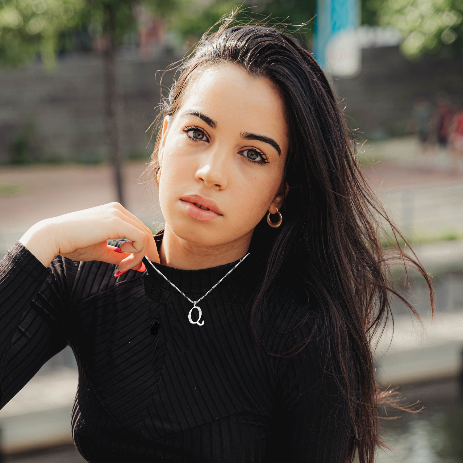 Woman wearing Q Necklace black ribbed sweater with a blurred outdoor background