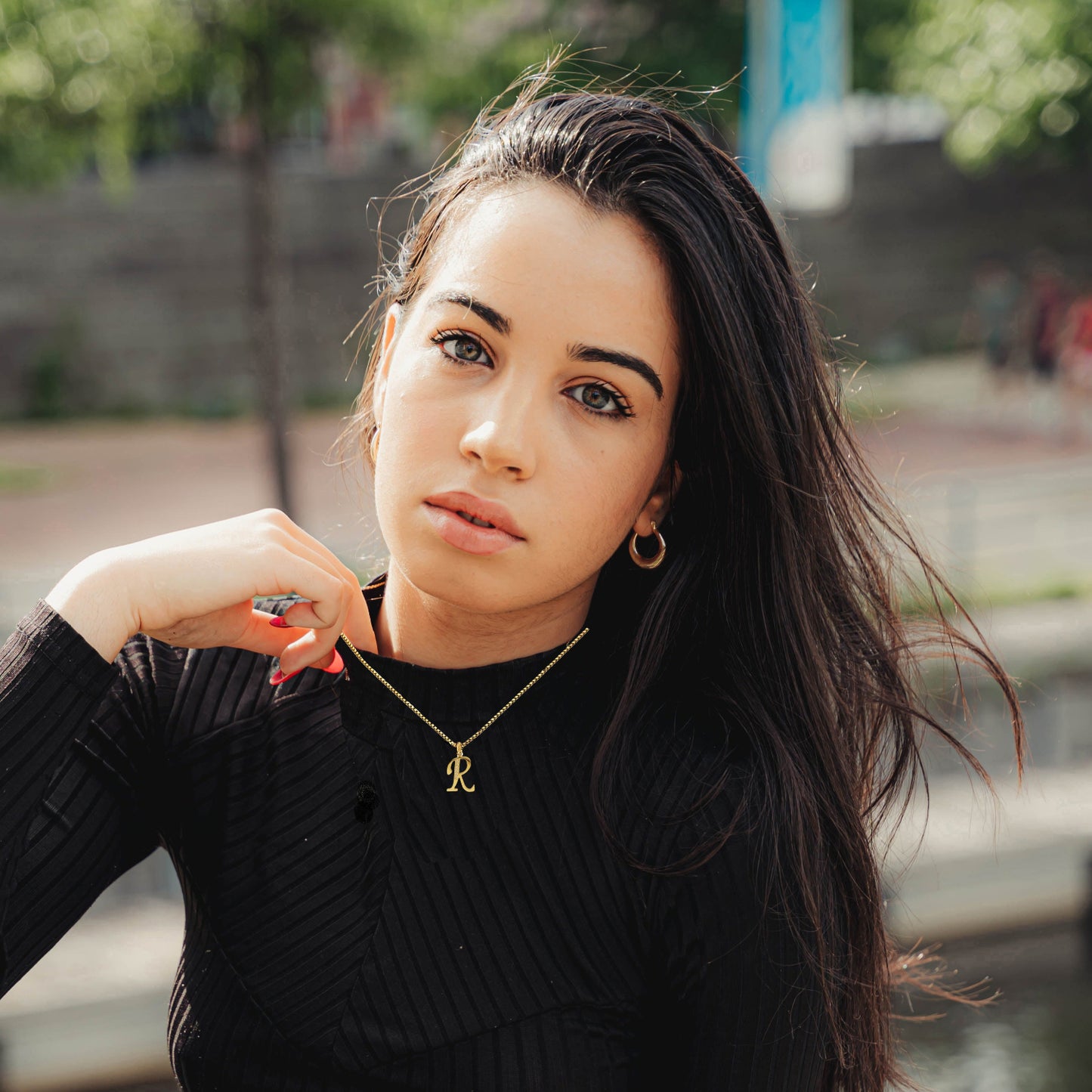 Woman wearing R Necklace black sweater with a blurred outdoor background