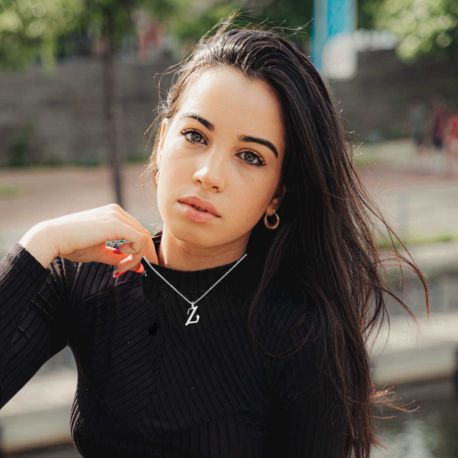 Woman wearing a Z Necklace black ribbed sweater with a blurred outdoor background