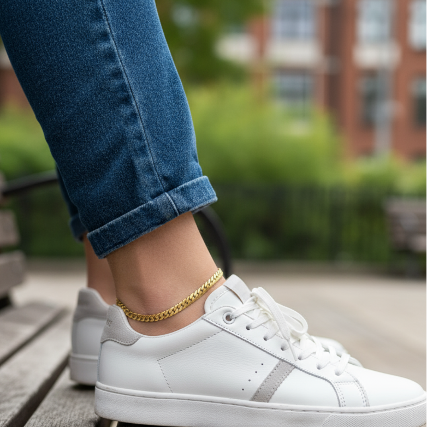 White sneakers worn with blue jeans on a wooden bench outdoors.