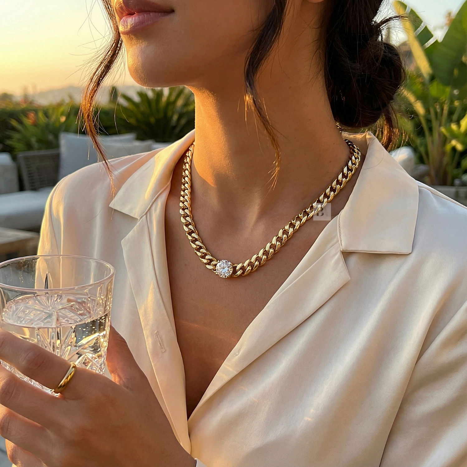 Woman wearing a gold chain necklace with a diamond pendant, holding a glass of water.