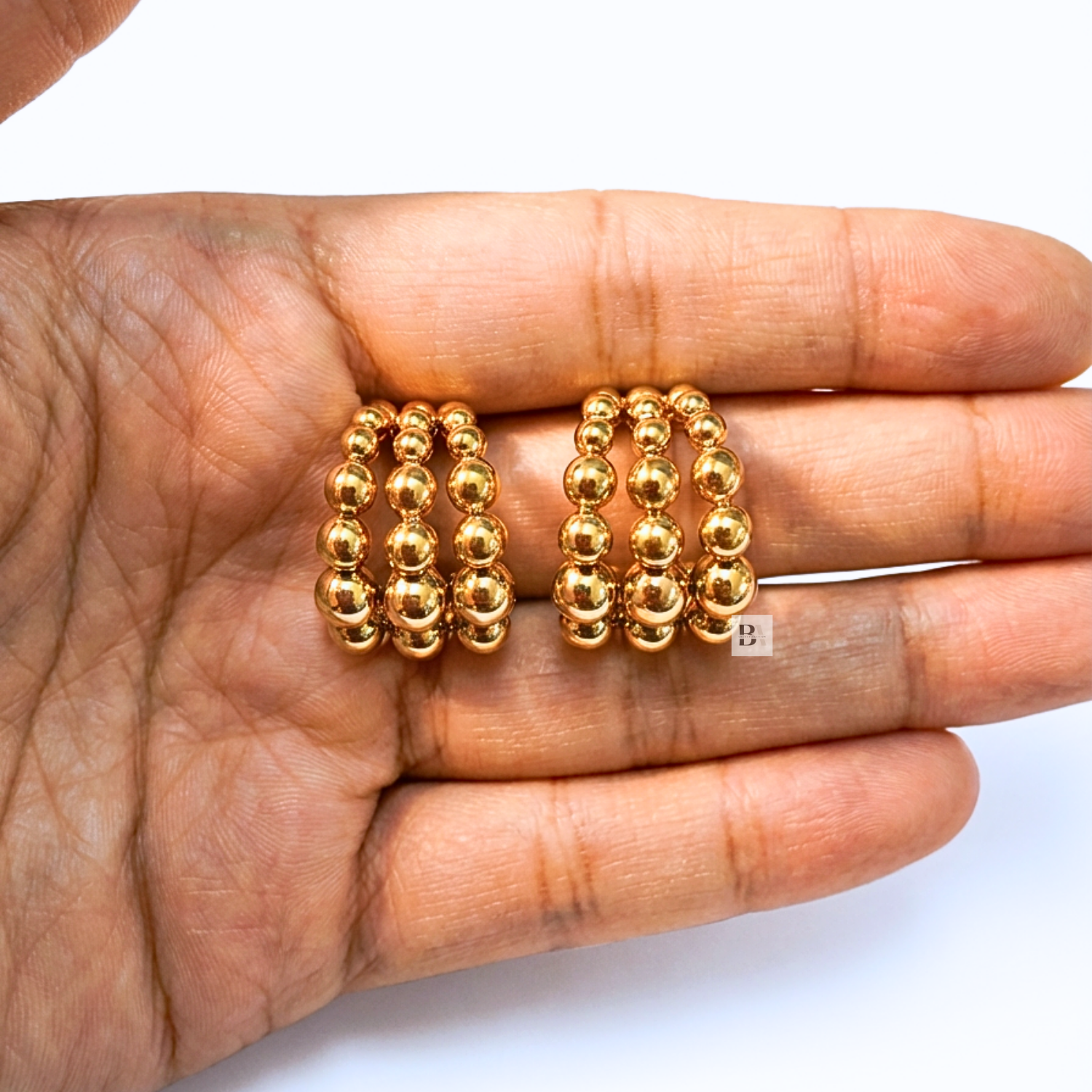 Gold hoop earrings held in a hand against a white background