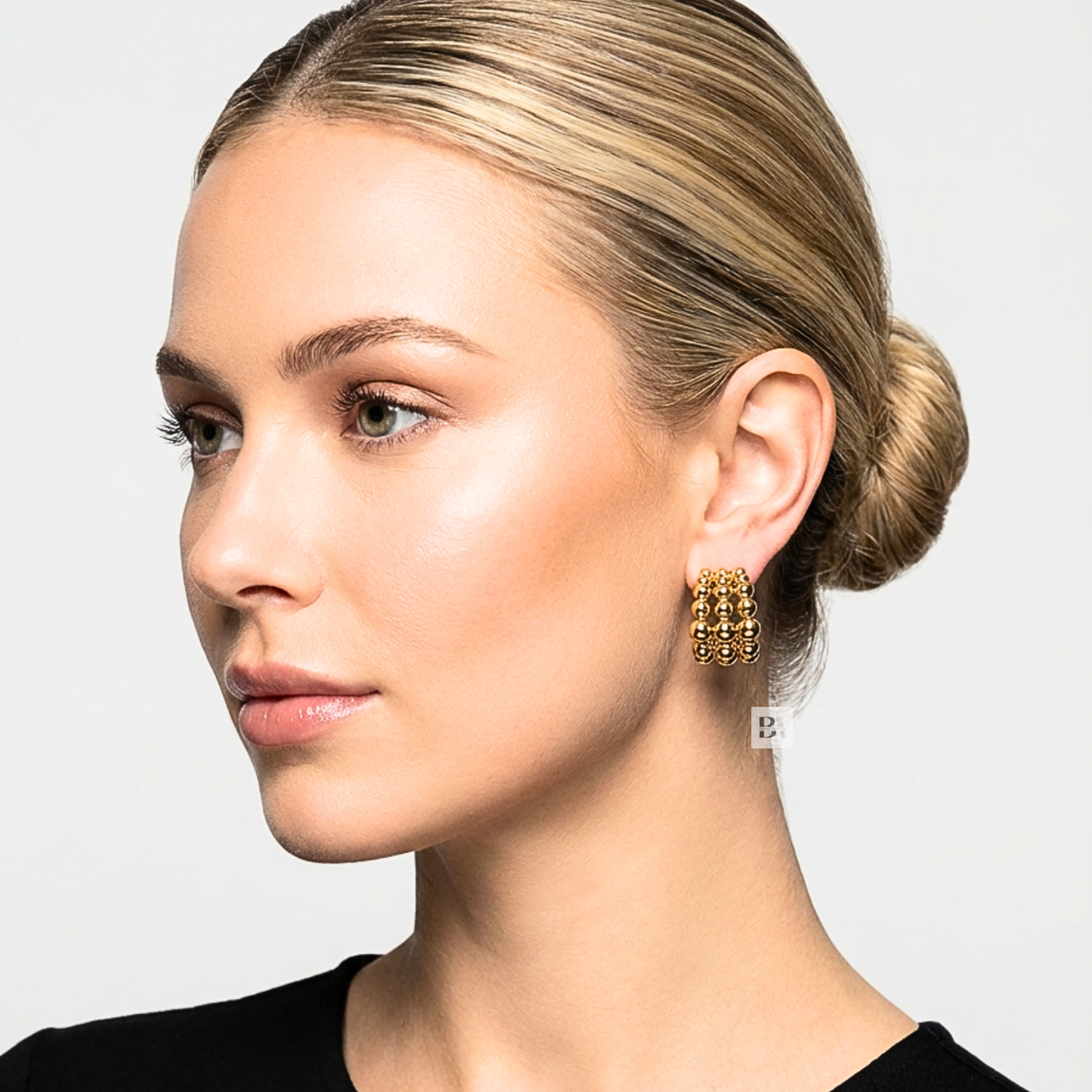 Close-up of a woman wearing gold hoop earrings with a neutral background