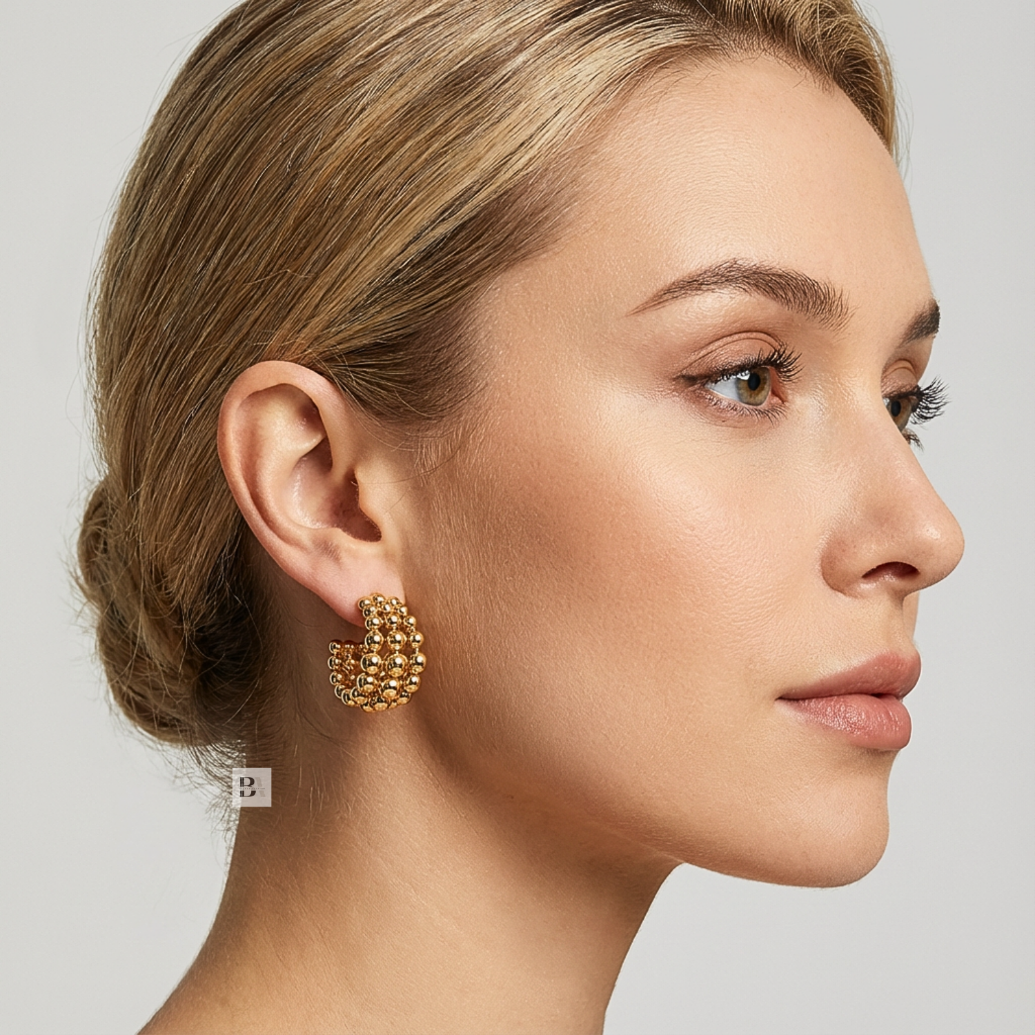 Close-up of a woman wearing gold earrings with a neutral background